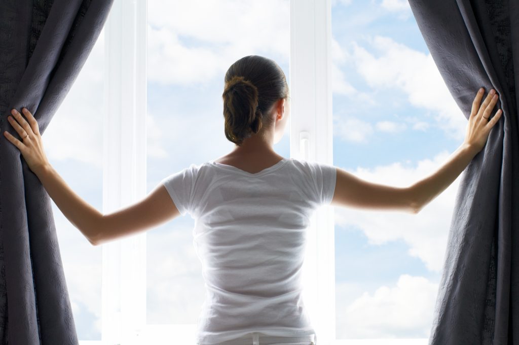 A woman opening her blinds to tan through her window image